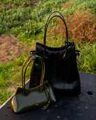 Black handbag and green handbag on a metal surface with grass in the background