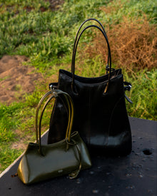 Black handbag and green handbag on a metal surface with grass in the background