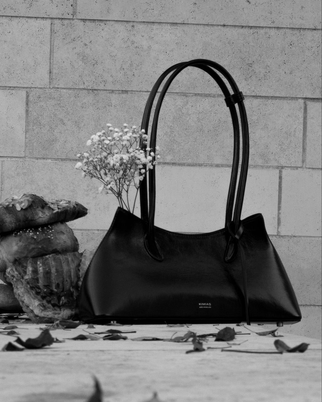 Black handbag and decorative items on a stone surface with a stone wall background